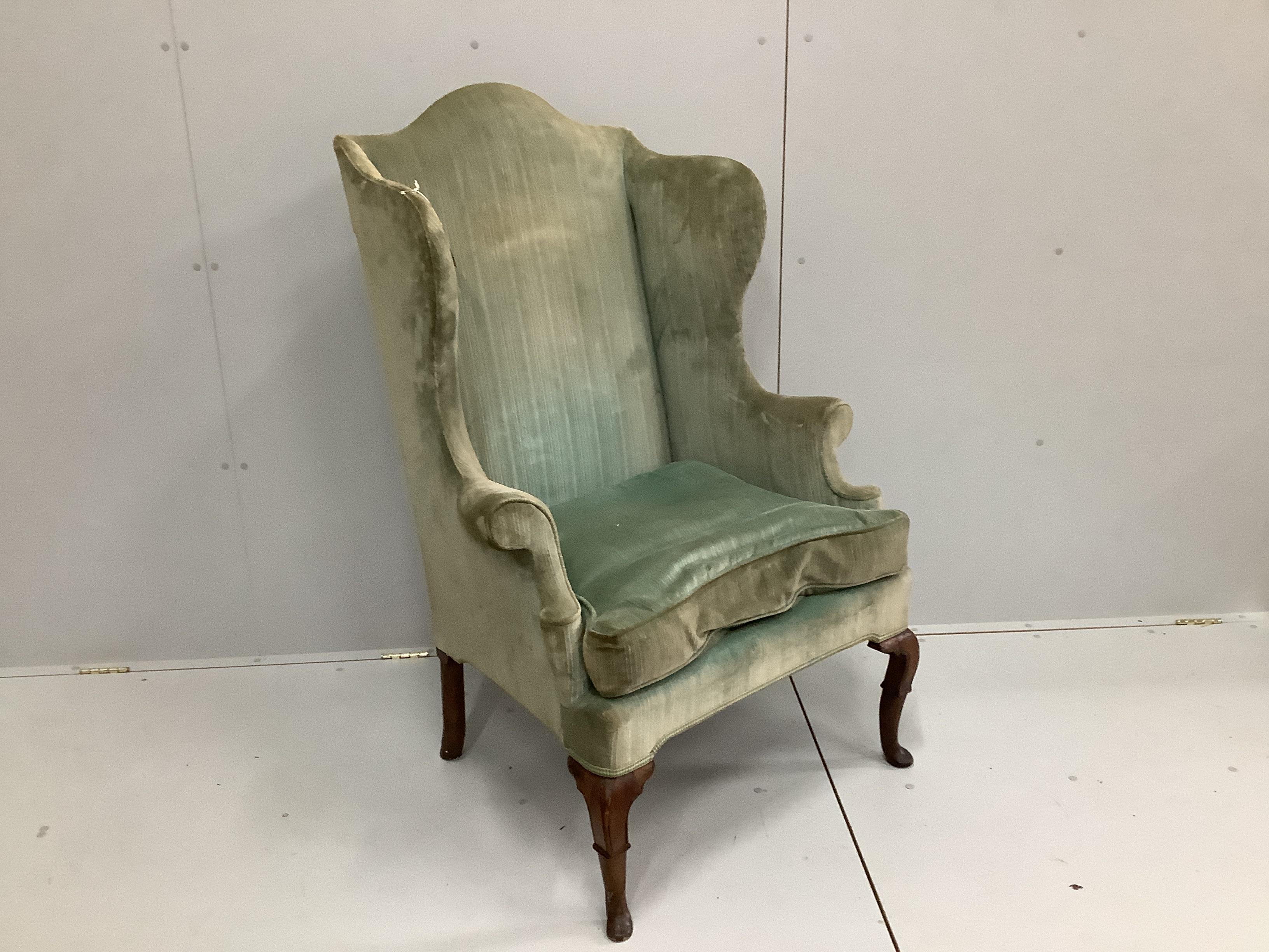 An 18th century upholstered wing armchair on carved walnut cabriole legs, width 80cm, depth 70cm, height 126cm.